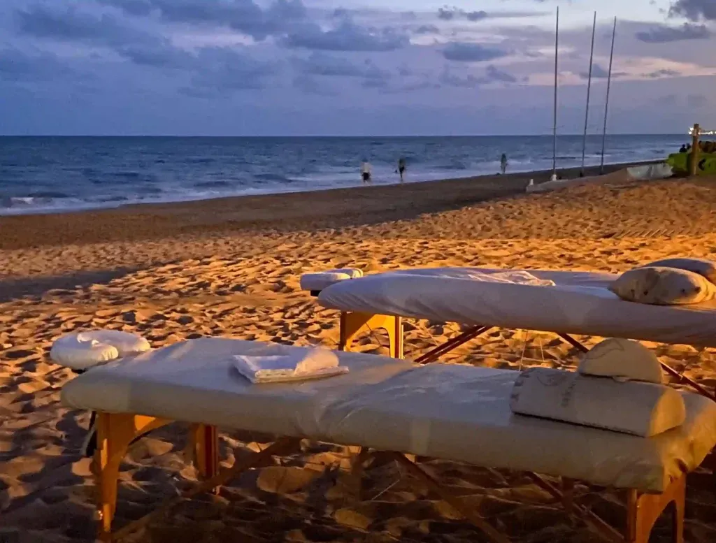 Dos camillas de Masaje Californiano sobre la arena frente el mar, preparadas para un masaje en pareja.